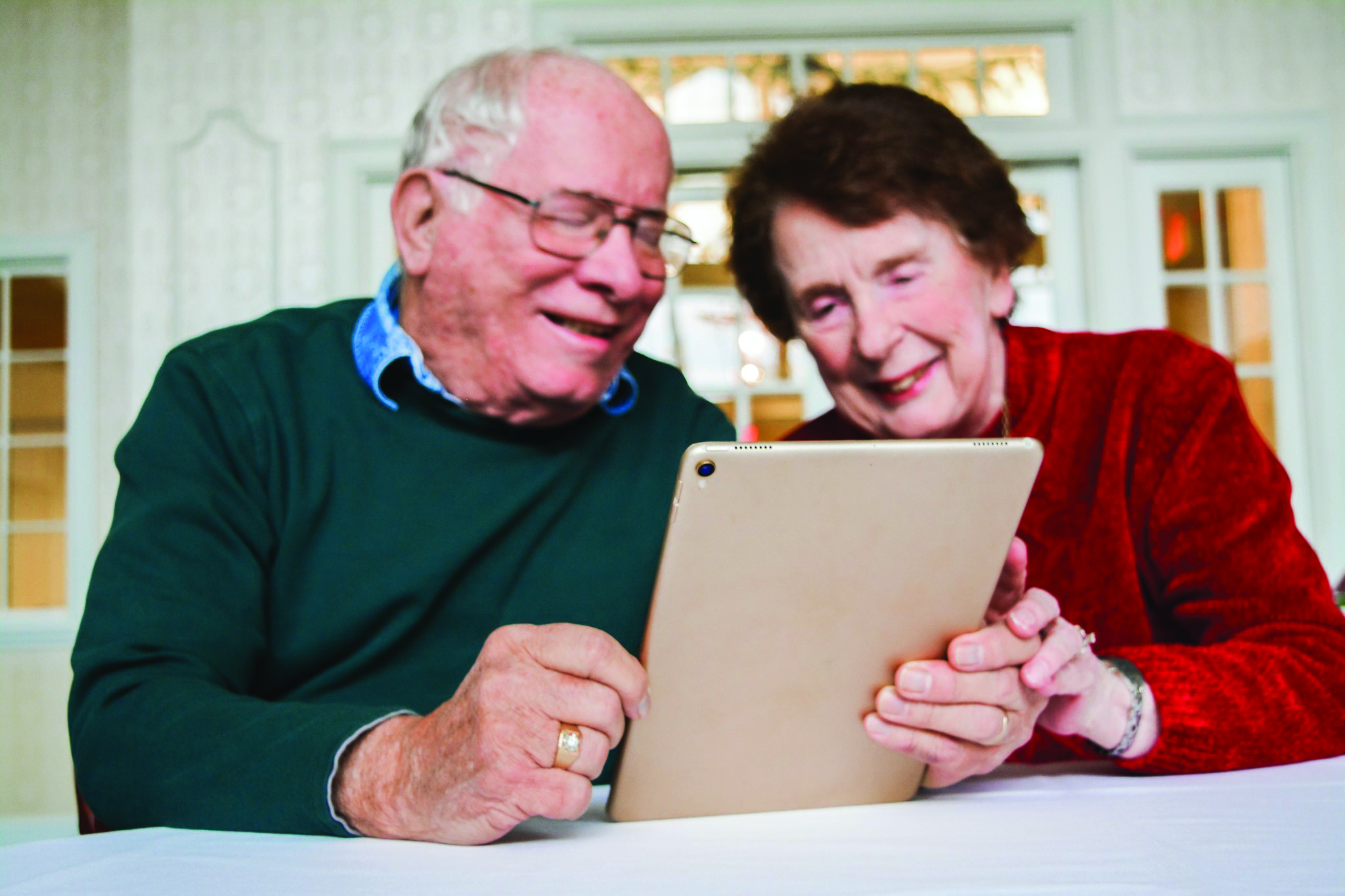 A resident couple at The Glenwood Community in Marietta, Ohio, huddles over their tablet with faces of joy. 