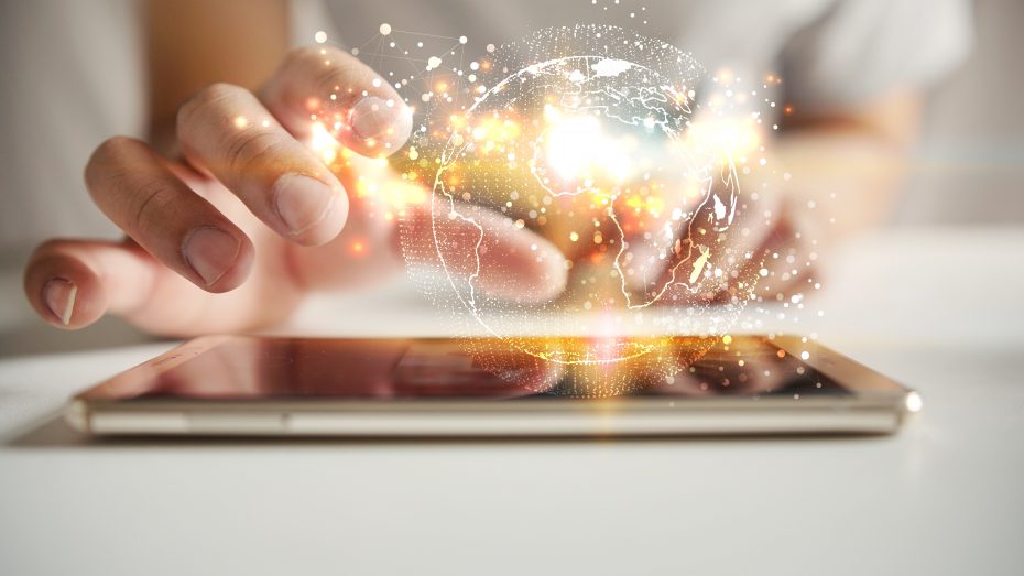 A person touches a tablet, with a glowing digital globe and bright light effects hovering above it, symbolizing global connectivity and technology.