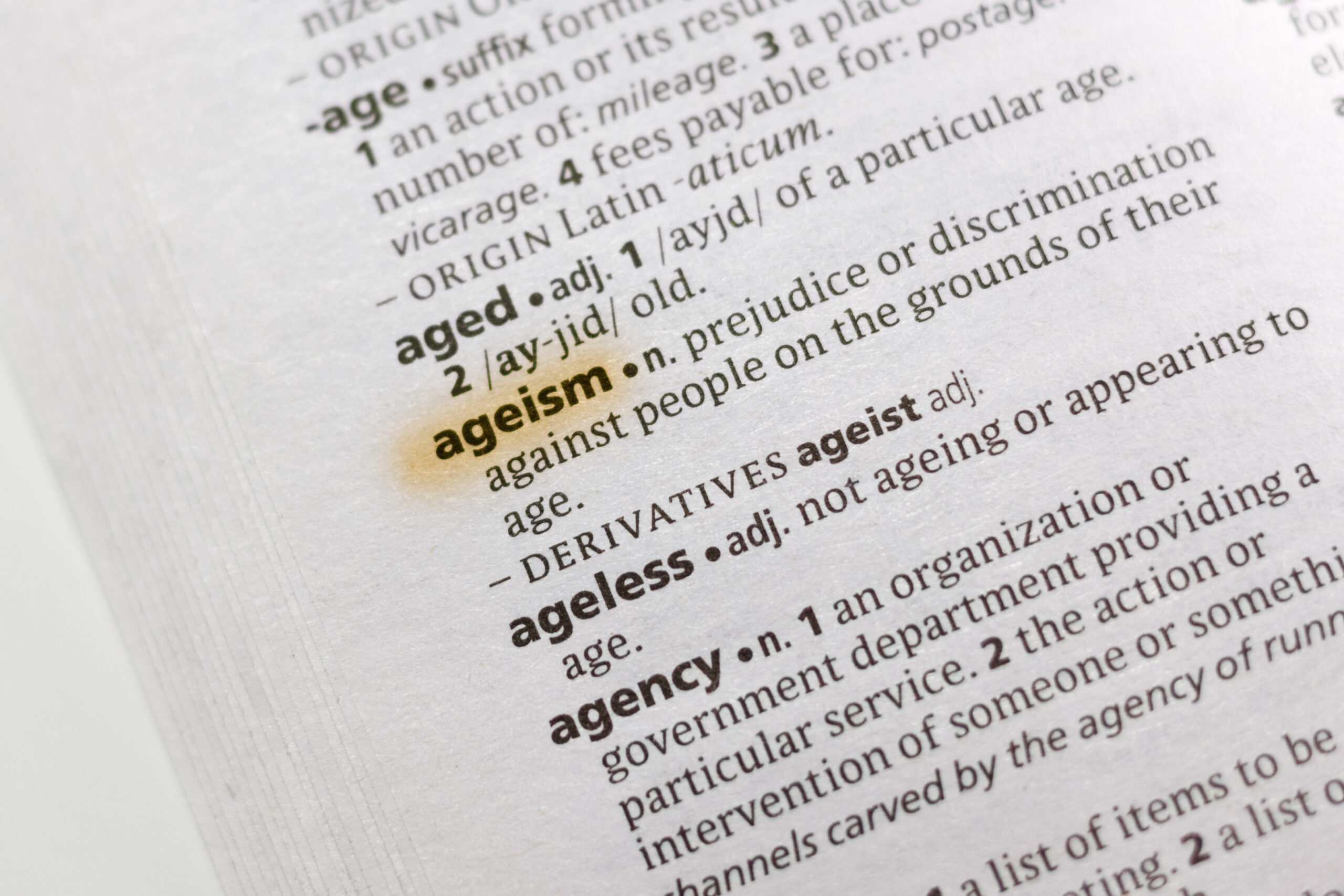 Close-up of a dictionary page highlighting the definition of the word "ageism," which refers to prejudice or discrimination against people based on their age.