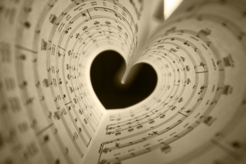 Sheet music pages curled to form a heart shape, with musical notes clearly visible. The image is in a sepia tone.