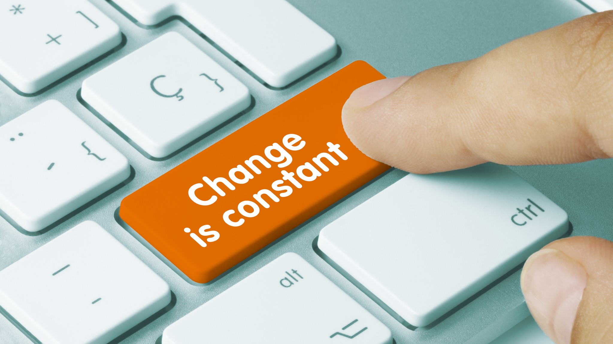 A finger presses an orange key labeled "Change is constant" on a white computer keyboard.