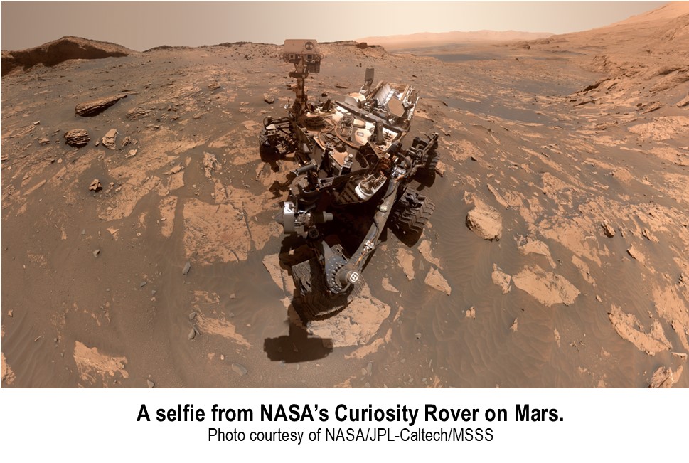 A selfie captured by NASA's Curiosity Rover on the rocky surface of Mars. The Martian landscape stretches into the distance. Photo courtesy of NASA/JPL-Caltech/MSSS.