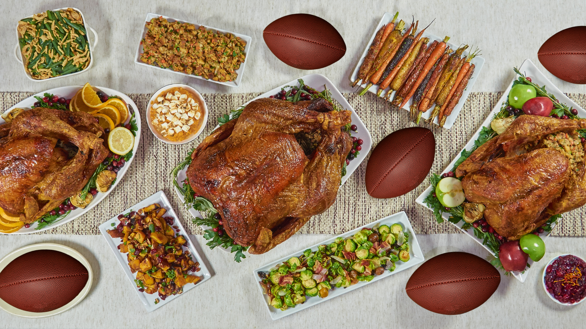 A table is set with Thanksgiving dishes including roast turkey, stuffing, green beans, carrots, dessert, and sides. Footballs are also placed among the food items.