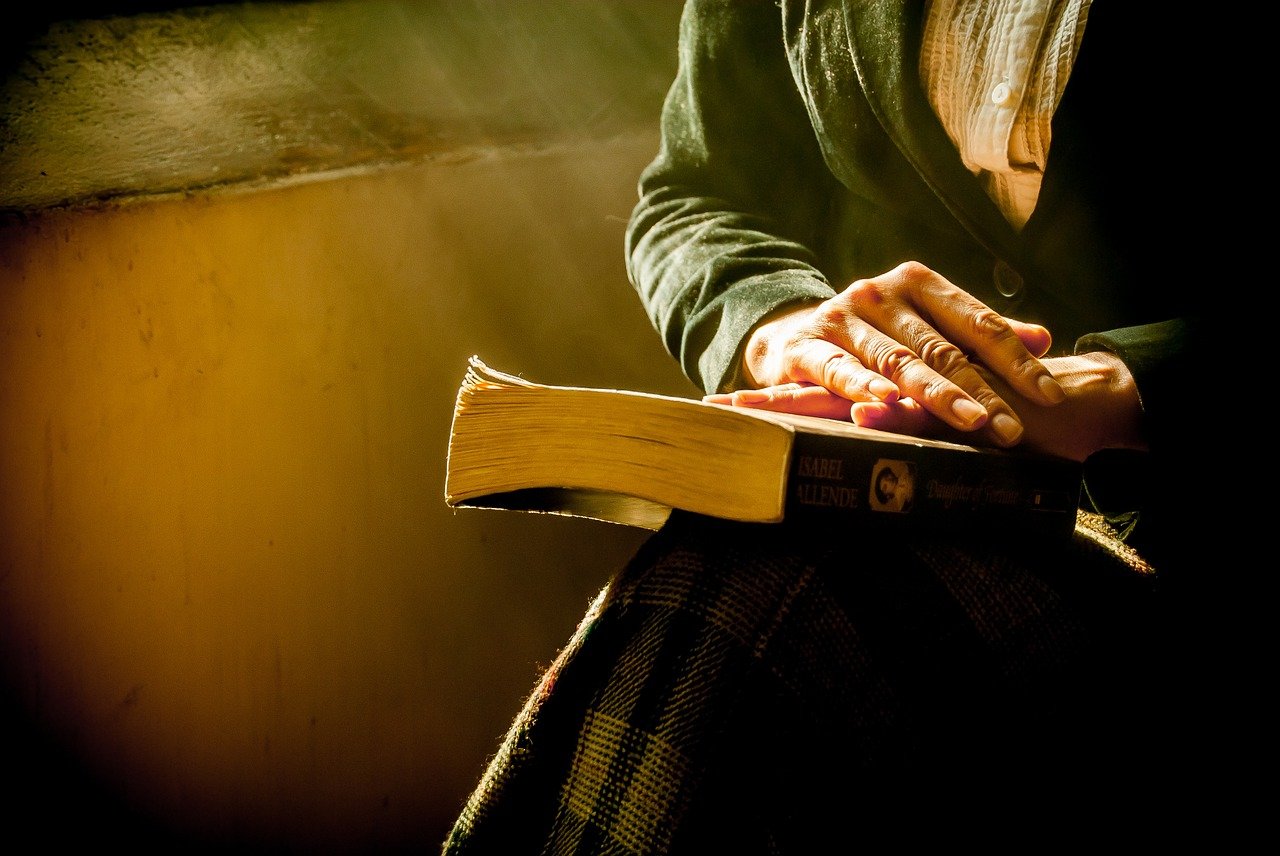 Person sitting with hands resting on an open book in soft, warm light.