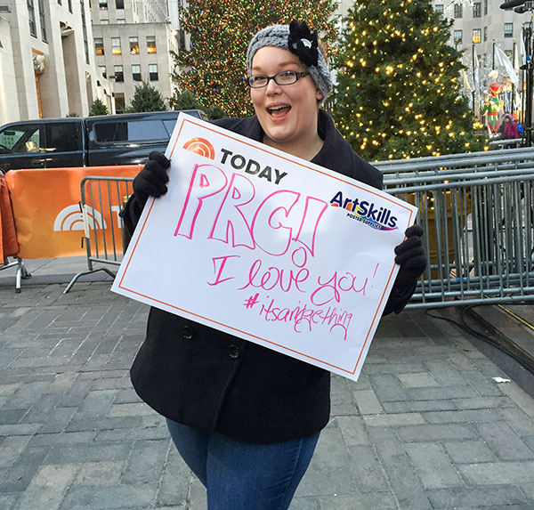 Casey Dukes standing on the set of the Today Show holding her sign