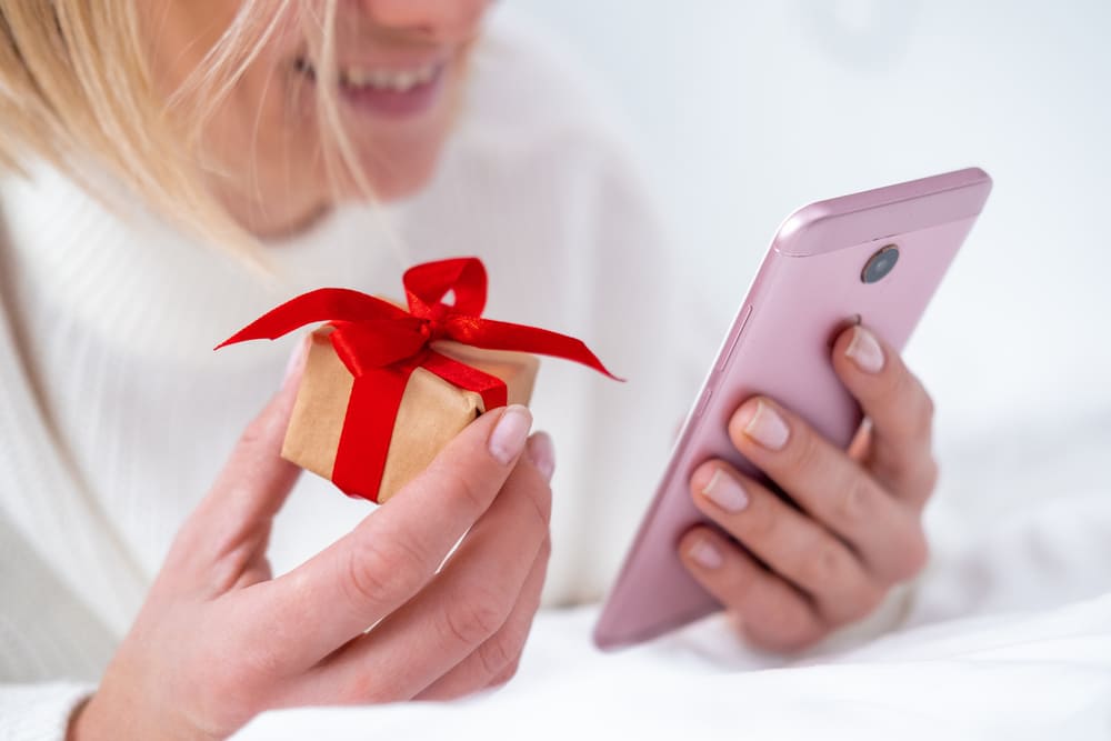 A person enjoying the uch career perks, holding a small gift with a red ribbon in one hand and a smartphone in the other, smiling.