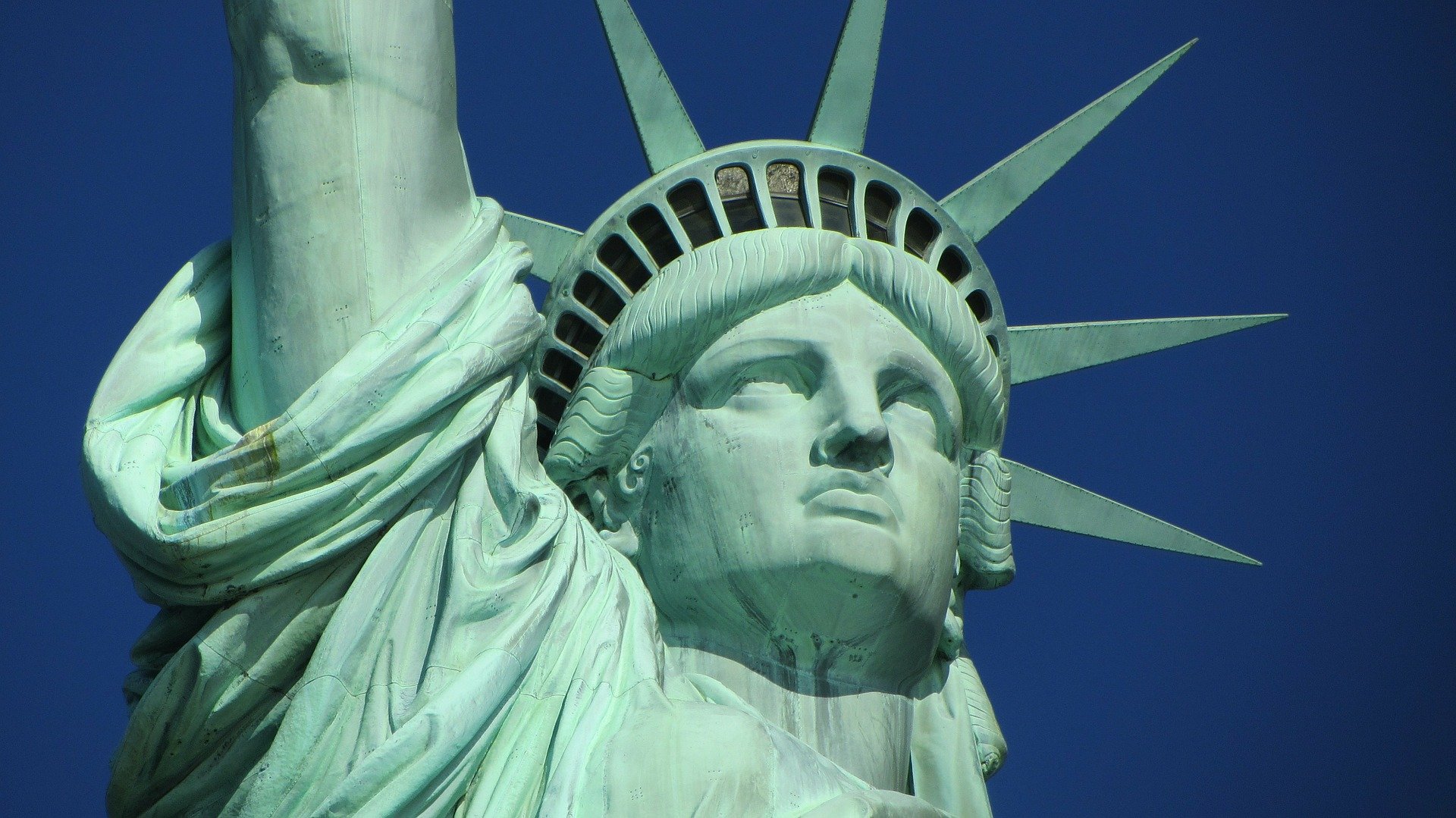 Close-up view of the upper portion of the Statue of Liberty, showing the face and crown against a clear blue sky.